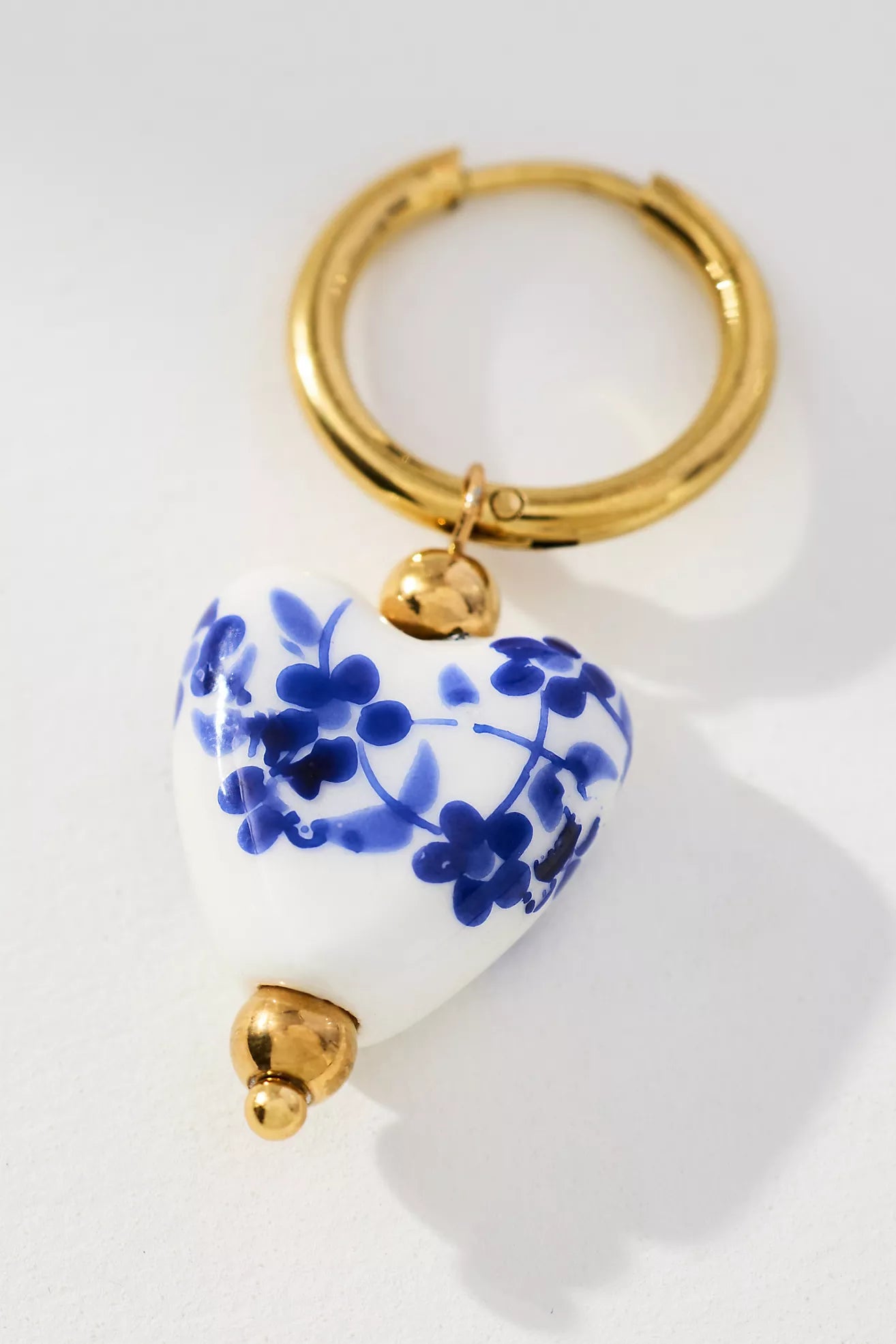 Gold hoop earring with a white heart-shaped keychain featuring blue floral patterns on a white background.