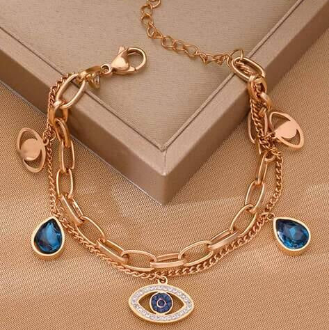 Gold bracelet with blue gemstones and an evil eye charm on a beige surface