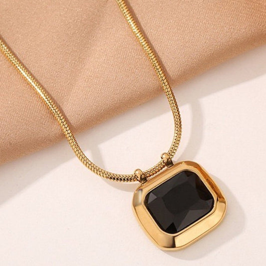 Gold necklace with a black pendant on a beige fabric background