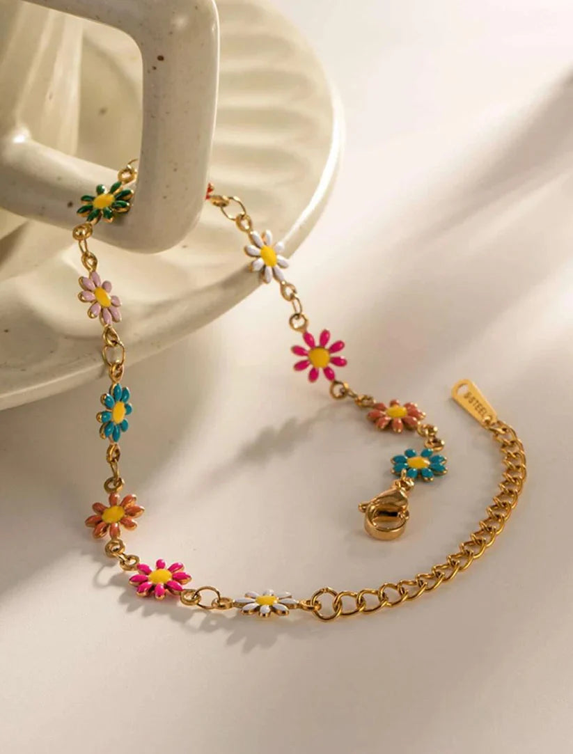 Gold bracelet with colorful flower charms on a white surface